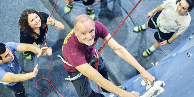 Actividades de team building en Madrid hombre escalando mientras el equipo acompaña Actividades de team building en Madrid hombre escalando mientras el equipo acompaña