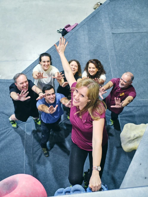 actividad de team building Madrid mujer escalando en rocódromo con su grupo que acompaña actividad de team building Madrid mujer escalando en rocódromo con su grupo que acompaña